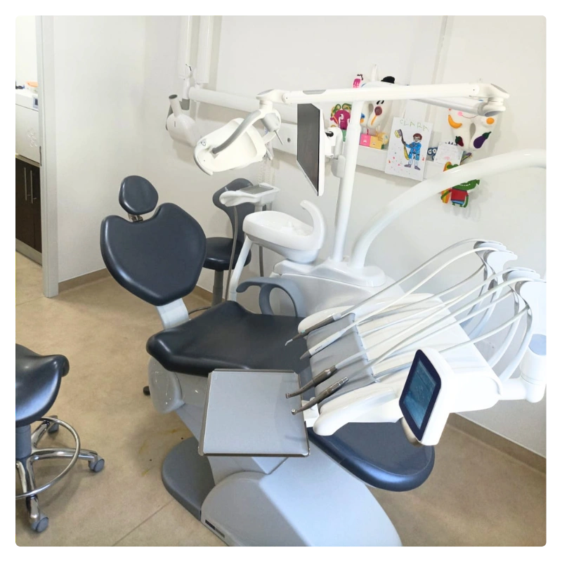Dental patient chair with overhead light, dental instruments, and monitor in a clinic treatment room.
